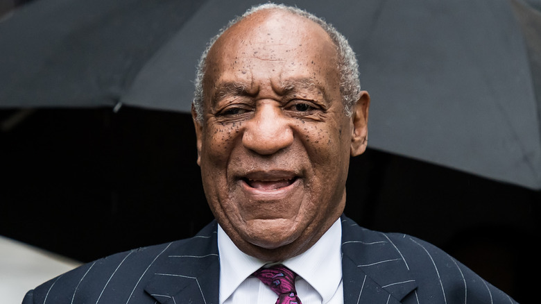 Bill Cosby smiling in pinstripe suit outside courthouse